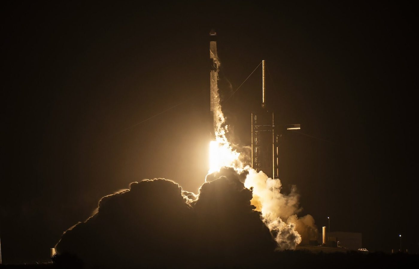SpaceX Falcon 9 rocket lifting off at night from Kennedy Space Center, lighting up a cloud of exhaust