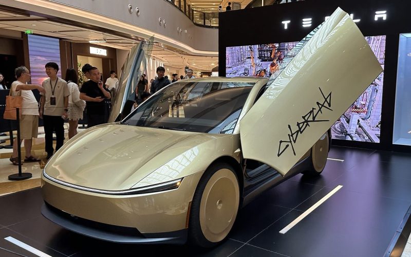 Gold Tesla Cybercab two-seat robotaxi with its butterfly door open on display inside a Tesla showroom