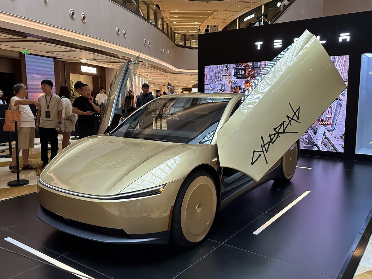 Gold Tesla Cybercab two-seat robotaxi with its butterfly door open on display inside a Tesla showroom