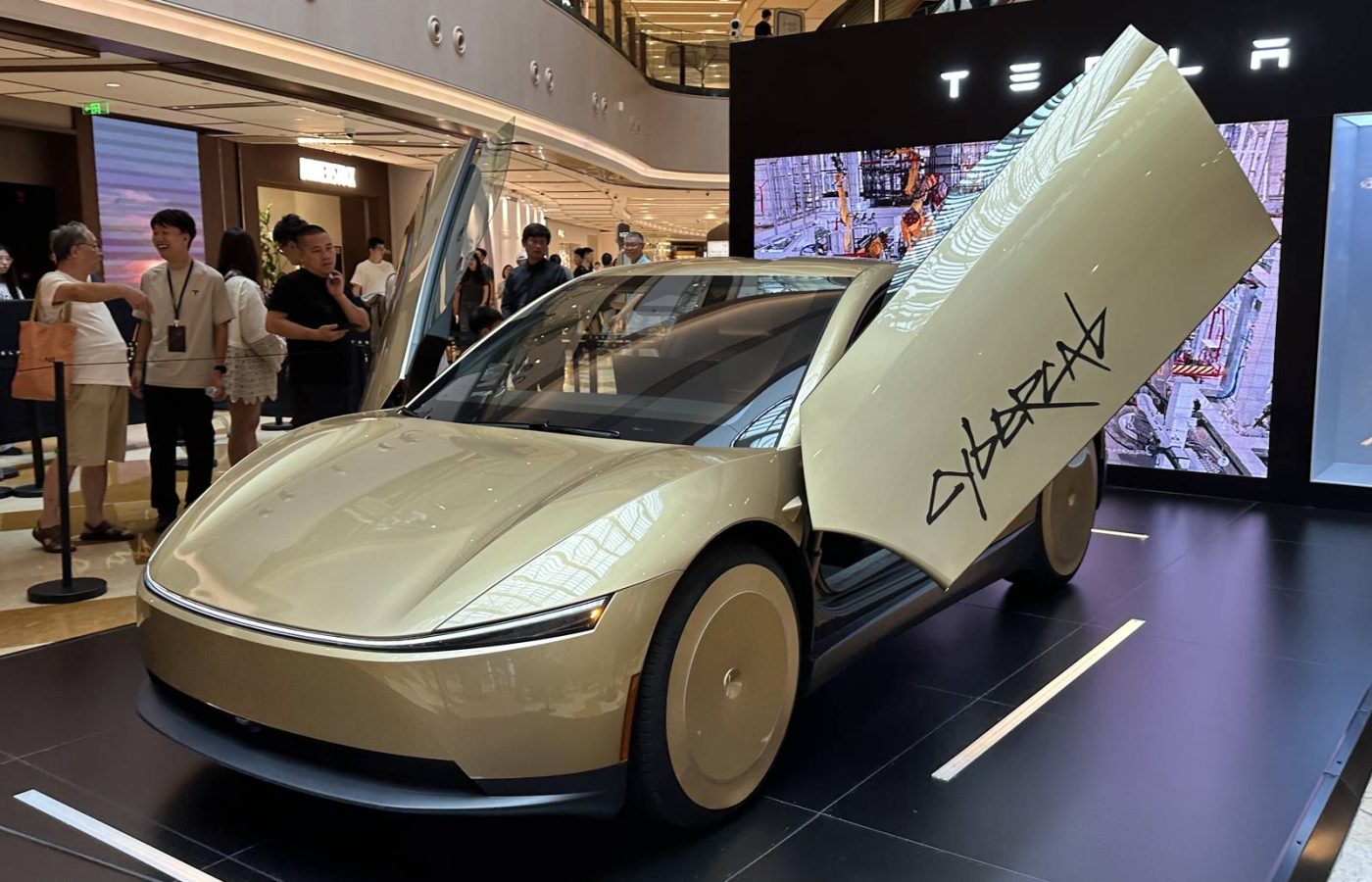 Gold two-seat Tesla Cybercab on display with its butterfly doors open and the Cybercab logo on the door.