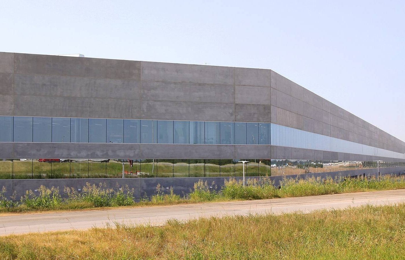Exterior of Tesla Gigafactory Texas, a long grey factory building with blue glass, in Austin