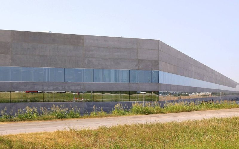 Exterior of Tesla Gigafactory Texas, a long grey factory building with blue glass, in Austin