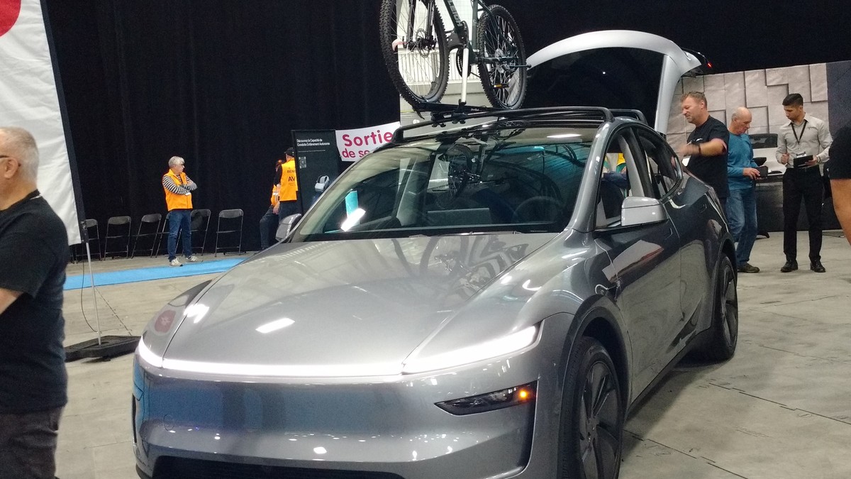 Silver 2025 Tesla Model Y with its rear liftgate open and a bike on the roof at an indoor auto show