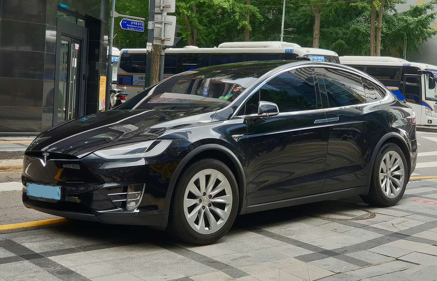 Black Tesla Model X SUV parked at a city curb, side and front view