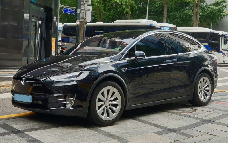 Black Tesla Model X SUV parked at a city curb, side and front view