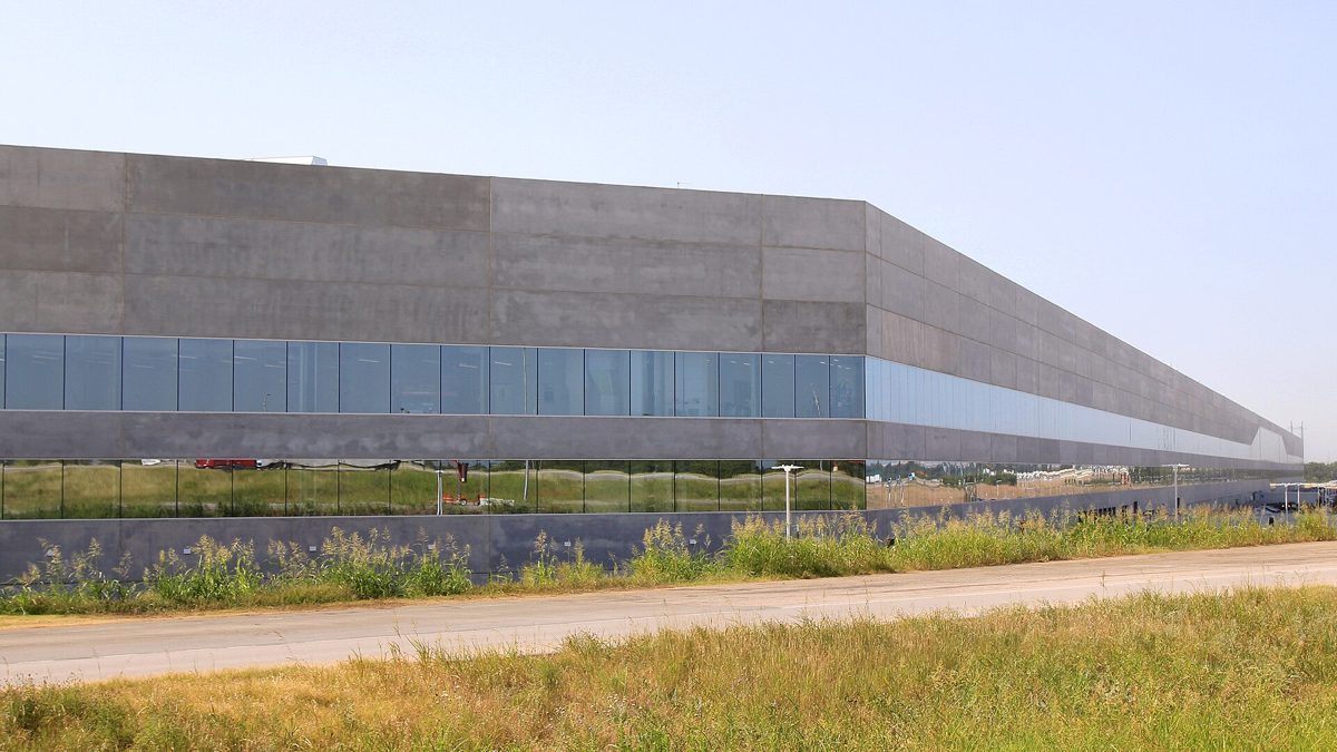 Long grey concrete and glass wall of Tesla Gigafactory Texas Building 1 near Austin under a clear sky