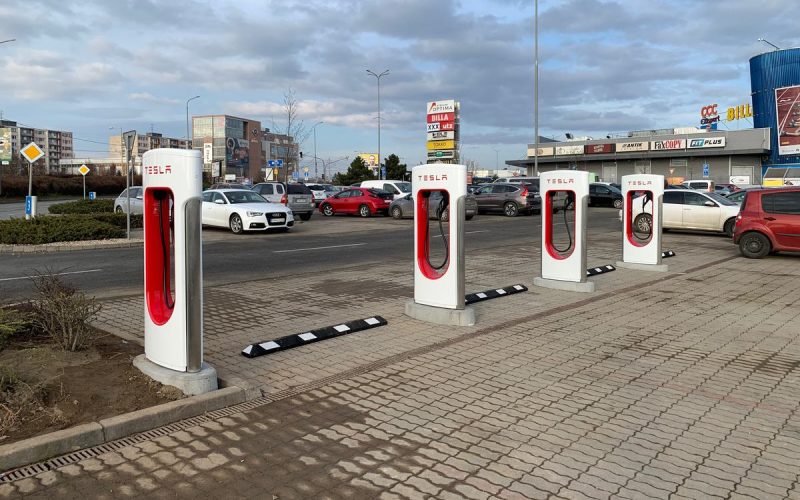 Four Tesla Supercharger stalls in a shopping centre parking lot in Košice, Slovakia, under a cloudy sky