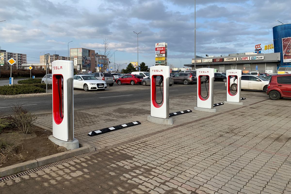 Four Tesla Supercharger stalls in a shopping centre parking lot in Košice, Slovakia, under a cloudy sky