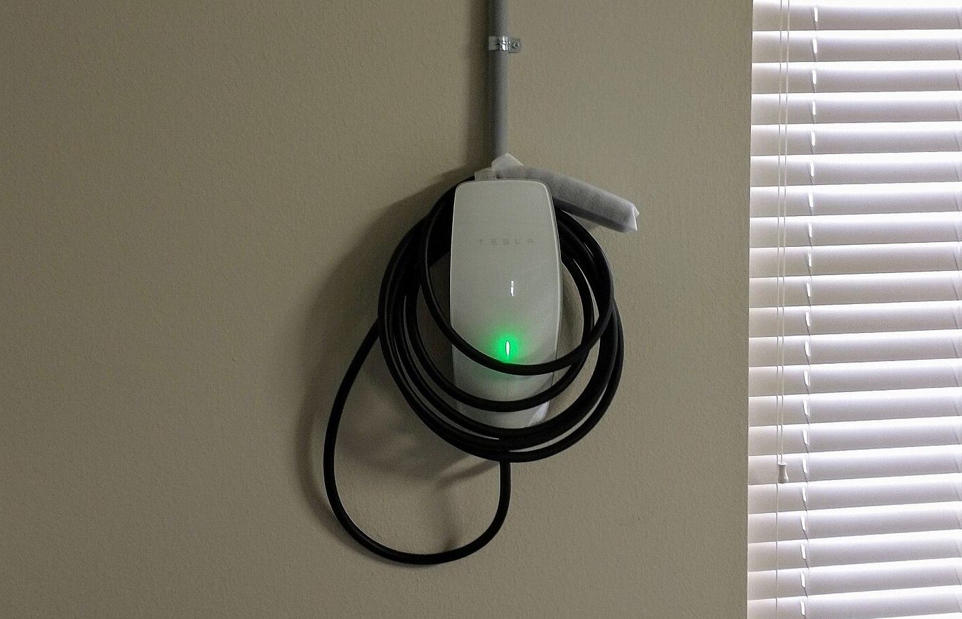Tesla Wall Connector mounted on a garage wall with its charging cable coiled