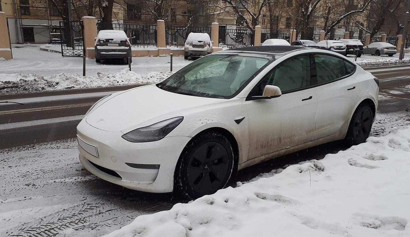 White Tesla Model 3 parked on a snowy city street in winter
