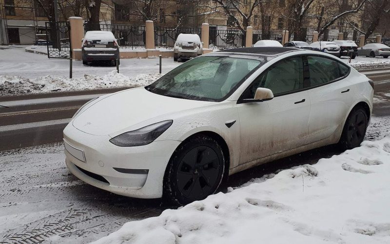 White Tesla Model 3 parked on a snowy city street in winter